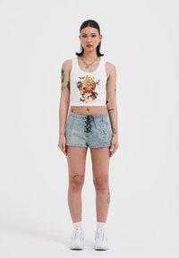 Top corto blanco con un diseño gráfico colorido, combinado con pantalones cortos de mezclilla azul claro con cordones en la parte frontal y bordados decorativos.