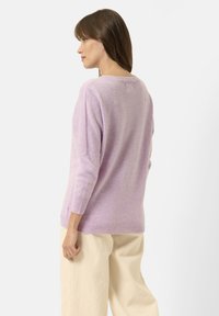 Pull en laine lavande avec un col rond, des manches 3/4 et une coupe décontractée. Le tissu a une finition douce et texturée. Un pantalon blanc complète le look.