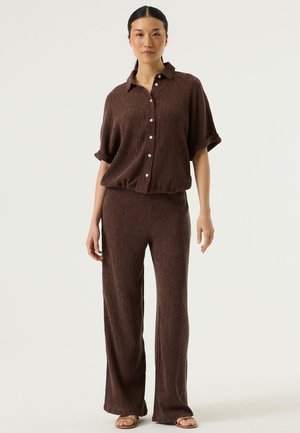 Bruin gestructureerd bijpassend set bestaande uit een kortärmelig overhemd met knopen en broek met wijde pijpen; stof heeft subtiele verticale lijnen.
