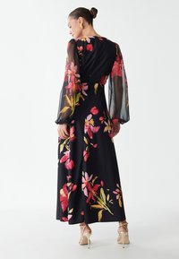 Abito maxi con maniche lunghe trasparenti, tessuto nero decorato con motivi floreali colorati in rosa, rosso e giallo. Silhouette fluida con una vita aderente.