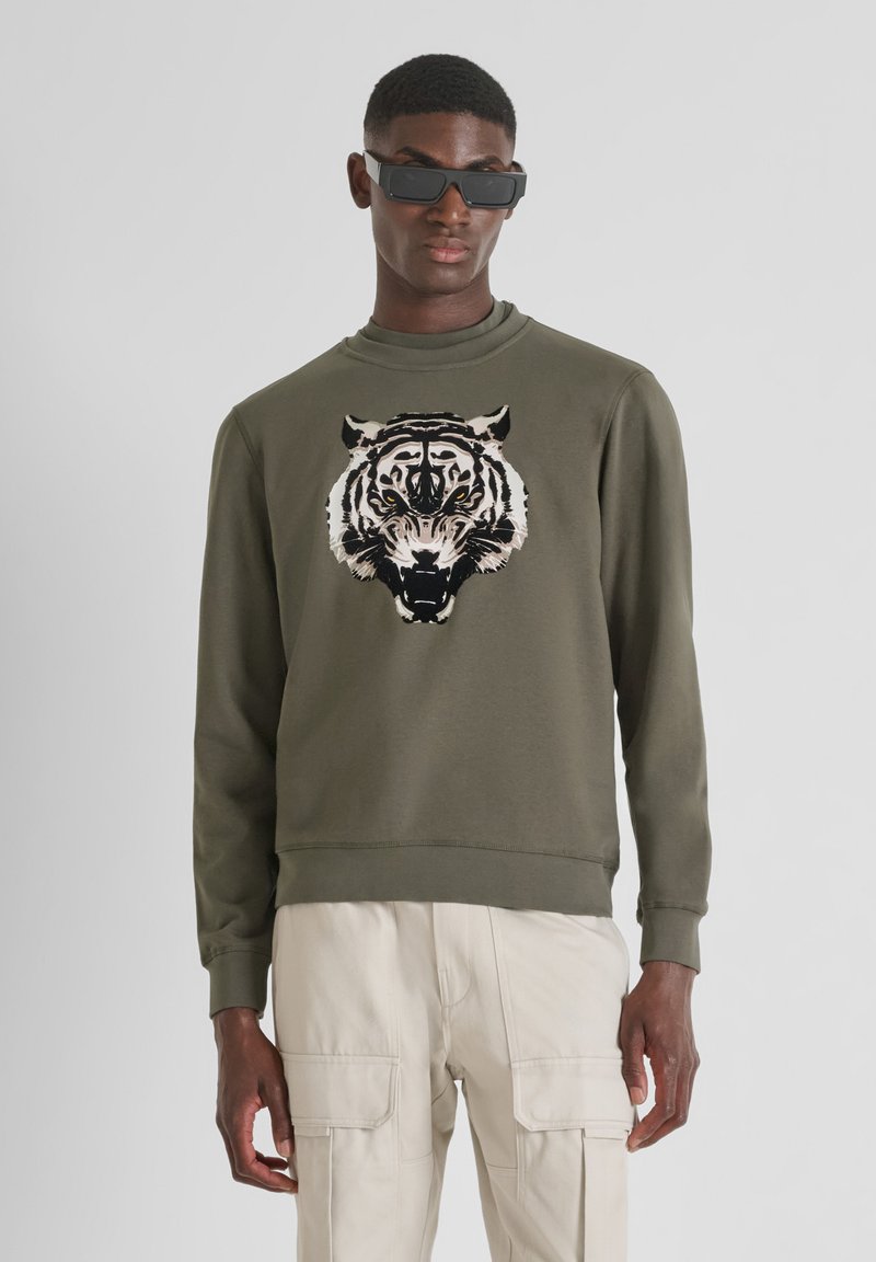 Sudadera verde oliva con cuello redondo y mangas largas, que presenta un gran gráfico de tigre en crema y negro en la parte frontal.