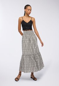 Top corto in pizzo nero abbinato a una gonna bianca con motivi a foglie nere, design a più strati e cintura elastica. Sandali neri con cinturini.