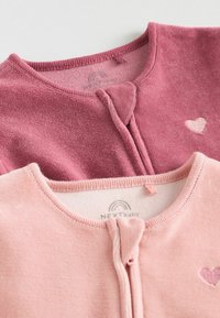 Dos cárdigans para bebé en una tela suave, uno en rosa oscuro con un corazón bordado, el otro en rosa claro con una cremallera frontal y cuello redondo.