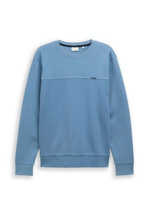 Niebieska bluza wykonana z miękkiego materiału, z teksturowaną górną częścią, długimi rękawami i okrągłym dekoltem. Małe logo przy dolnej krawędzi.