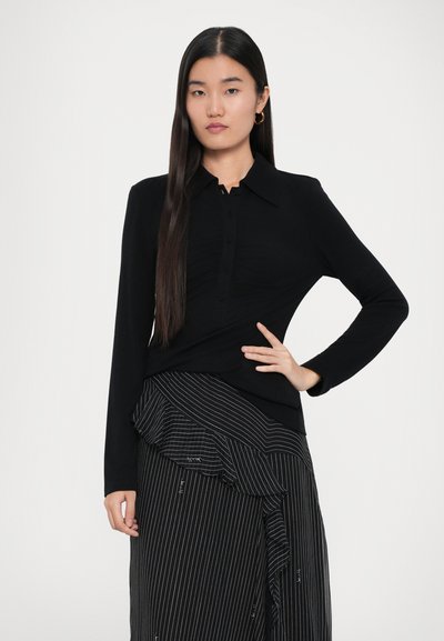 Top negro de manga larga con cuello y botón, combinado con una falda a rayas en blanco y negro con un dobladillo con volantes.