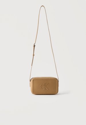 Petit sac bandoulière rectangulaire en cuir couleur tan avec sangle réglable et logo "cK" embossé sur le panneau avant.