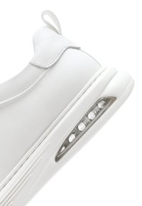 Scarpa sportiva bianca con una tomaia sintetica liscia, suola testurizzata e un cuscino d'aria visibile nella zona del tallone.