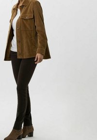 Chaqueta de pana marrón con bolsillos en el pecho, combinada con pantalones ajustados marrón oscuro. El modelo lleva una camiseta blanca debajo.