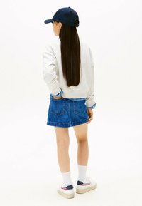 Sudadera gris, falda de mezclilla azul, calcetines blancos y zapatos. Pelo largo peinado suelto, gorra navy llevada hacia atrás. Atuendo simple y casual.