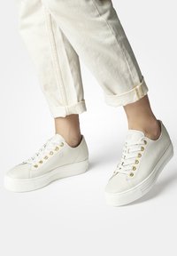 Baskets en cuir blanc avec une finition texturée, œillets dorés et semelle surélevée. Présente un design simple et arrondi avec un laçage à l'avant.
