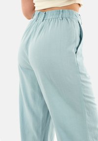 Pantaloni ampi di colore blu chiaro, con vita elasticizzata e tasche laterali, realizzati in un tessuto morbido e leggero con una superficie liscia.