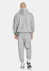 Szary, oversize'owy zestaw dresowy z kapturem i spodniami dresowymi, wykonany z miękkiej bawełny, z prążkowanymi mankietami i frontową kieszenią typu kangurka, zestawiony z białymi sneakersami.