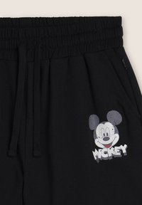 Pantaloni della tuta neri con vita elastica e cordini, caratterizzati da un volto di Topolino in stile usurato e il testo "MICKEY" nella zona della tasca anteriore.