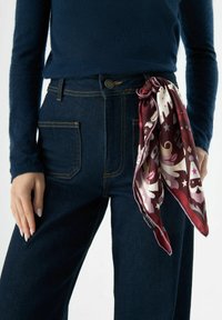 Zijden sjaal met een bordeauxrode basis en crèmekleurige en roze decoratieve patronen. Gecombineerd met donkerblauwe, hoogtaills jeans van denim en een marineblauwe top.
