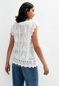Witte kanten blouse met gegolfde mouwen, bloemenborduursel en een gehaakte zoom, gecombineerd met loszittende blauwe jeans.