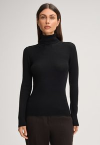 Zwarte geribbelde turtleneck trui met lange mouwen, een getailleerd ontwerp en een zachte textuur. Gestoeld met hoge taille donkere broeken.