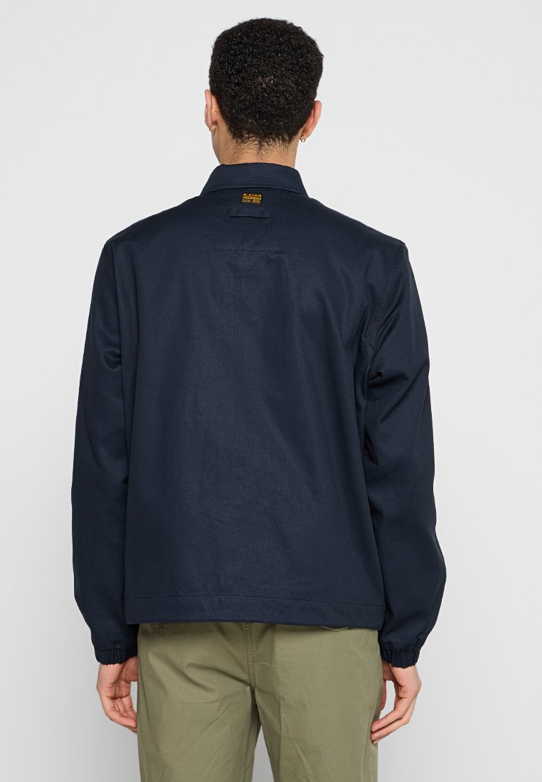 Marineblauwe jak gemaakt van gestructureerde stof, met een kraag, lange mouwen en elastische manchetten, voorzien van een klein logolabel aan de achterkant.