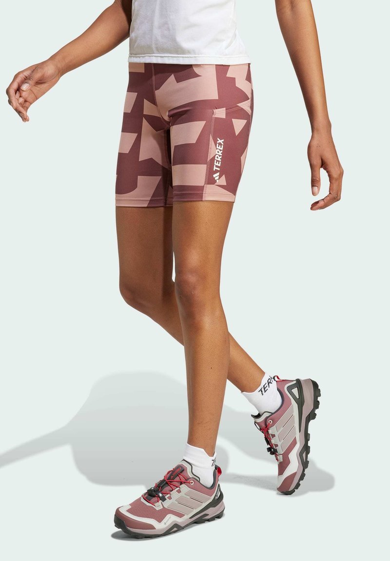 Lightweight, patterned shorts in shades of pink and beige with a side logo. Paired with multi-colored hiking shoes and white ankle socks.