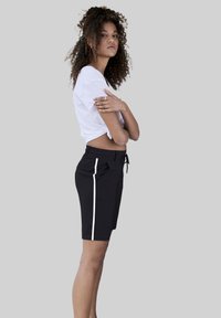 Black shorts with a drawstring waist, featuring white side stripes. The fabric appears smooth and lightweight. Worn with a cropped white top.