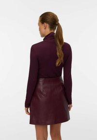 Bordeaux coltrui gecombineerd met een donkere bordeaux leren minirok. Glad stofoppervlak met een nauwsluitend ontwerp en subtiele stikdetails.