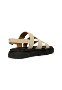 Beige suede sandal with wide straps, adjustable buckle, and black rubber sole. Features a cushioned insole and a rectangular toe shape.