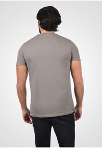 Camiseta gris de manga corta con cuello redondo, hecha de algodón suave, con un corte ajustado y costuras planas, llevada con jeans oscuros.