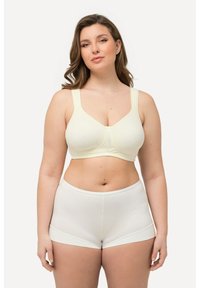 Sujetador inalámbrico de color amarillo claro con tirantes anchos y copas suaves, combinado con bóxer blancos sin costuras, ambos diseñados para la comodidad.