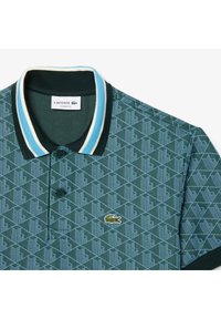 Grön polo skjorta med ett geometriskt mönster, med en tvåfärgad randig krage, två knappar och en liten broderad logotyp på bröstet.