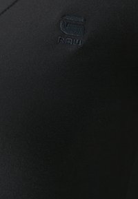 Černá tkanina s jemně vyšitým logem, které obsahuje abstraktní design a text "RAW" v tmavé nitě.