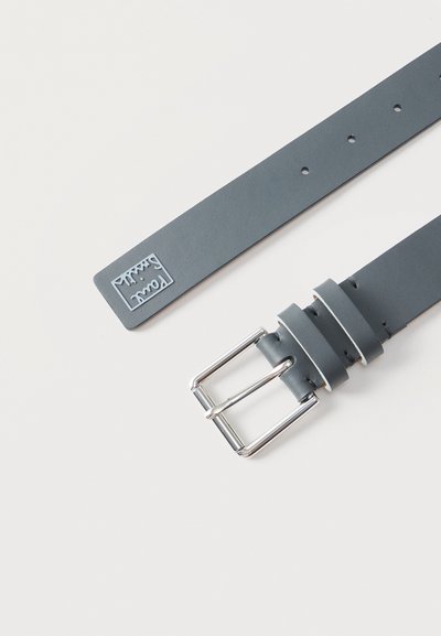 Σκούρα γκρι δερμάτινη ζώνη με ασημί ορθογώνιο αγκράφα και μικρό ανάγλυφο λογότυπο κοντά σε ένα άκρο, εμφανισμένη επίπεδη σε λευκό φόντο.