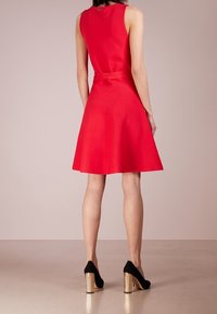 Punainen hihaton mekko, jossa on istuva bodice ja leveä hame, ja siinä on matching vyö. Mustat korkokengät, joissa on kultaiset yksityiskohdat.