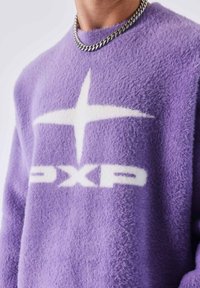 Suéter morado de felpa con una gran estrella blanca y el logo "PXP". La textura es suave, con un cuello redondo y mangas largas.