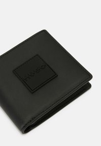 Carteira de couro preto com uma superfície texturizada e um logótipo preto em relevo em destaque. Design compacto com bordas cosidas.