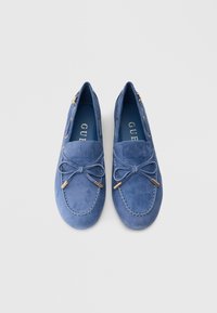 Sinised seemisnahast mokassiinid ümarate varvastega, dekoratiivse lipsuga, kulds toonis detailidega ja siledast nahast sisevoodriga, mille sees on brändi logo.