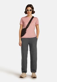 Camiseta cortas de manga rosa claro, pantalones de chándal gris oscuro, bolso cruzado negro y zapatillas beiges. Gafas de sol estilo ojos de gato blancas. Conjunto casual.