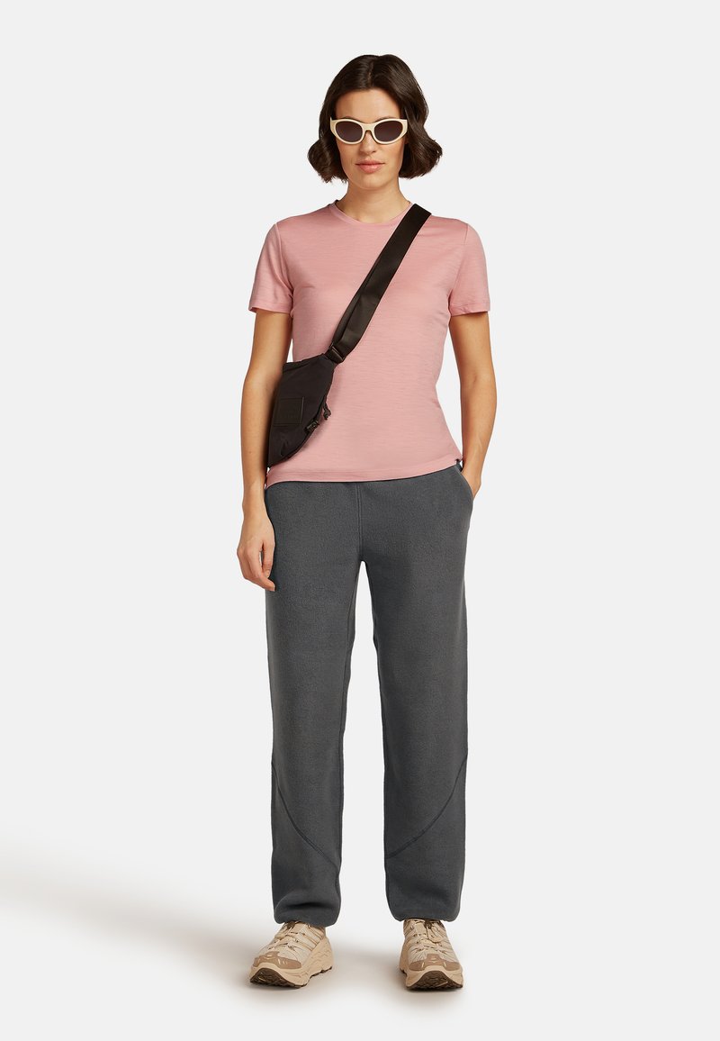 Camiseta cortas de manga rosa claro, pantalones de chándal gris oscuro, bolso cruzado negro y zapatillas beiges. Gafas de sol estilo ojos de gato blancas. Conjunto casual.