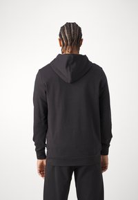 Sudadera negra con capucha que presenta un ajuste holgado, puños y dobladillo acanalados. Tejido suave con un diseño sin costuras en la espalda.