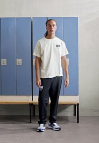 White cotton t-shirt with "1894" printed on the chest, paired with black sweatpants featuring a white graphic, and white-blue athletic shoes.