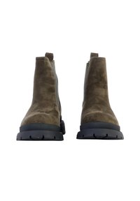 Botas de tobillo de ante marrón con una textura suave, lengüetas para facilitar el calce y suelas de goma negras con un patrón de tracción para un mejor agarre.
