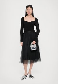 Zwarte off-shoulder top gecombineerd met een zwarte tule rok. Zilveren metallic schoenen. Kleine, bedrukte handtas met een opvallende vorm.