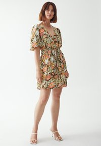 Floral dress in green, orange, and white with a v-neck and elastic waist. Short puff sleeves and a relaxed fit. Smooth fabric texture.