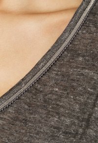 Tessuto grigio con una finitura testurizzata, dotato di scollatura arrotondata e una zip metallica visibile lungo il bordo.
