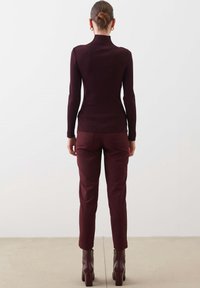 Burgundy ribbed turtleneck neule, fitted muotoilu, yhdistettynä yhteensopiviin burgundy tapered-housuihin, korostettuna paksupohjaisilla nilkkakengillä.