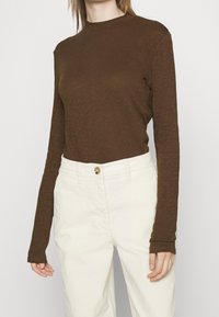 Bruine lange mouwen top in een textuurstof, met een hoge halslijn en aansluitende mouwen, gecombineerd met crèmekleurige hoge taillebroeken.