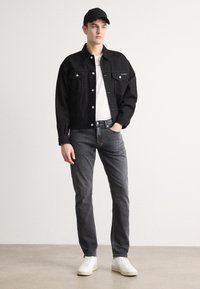 Črna denim jakna s srebrnimi gumbi, bela majica, sivi kavbojki in bele superge. Obleko dopolnjuje črna kapa.
