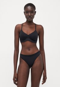 Svart bikiniset med en sömlös bralette med tunna axelband och matchande högmidjade trosor. Slät tyg med minimal detaljering.