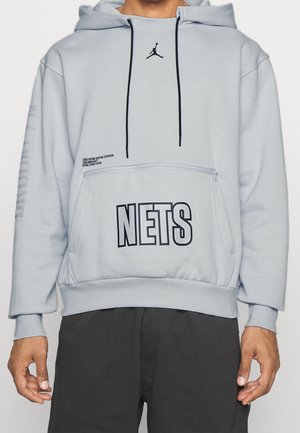 Jasnoszara bluza z kapturem z czarnymi sznurkami, czarne logo Jumpman, napis "NETS" nadrukowany na przedniej kieszeni oraz słabo widoczny napis "BROOKLYN" na rękawie.