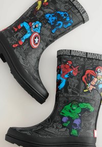 Mustat kumisaappaat, joissa on Marvel-sankareiden grafiikkaa, mukaan lukien Spider-Man ja Hulk. Taustalla on teksturoitu sarjakuvakirja-efekti ja erottuvat pohjat.