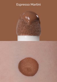 Bruine vloeistof bovenop een gestructureerde sponsapplicator, met een veeg op de huid eronder, die een rijke espresso kleur en een gladde afwerking toont.