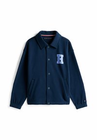 Giacca blu navy con bottoni e colletto, due tasche laterali, polsini elasticizzati e una grande "H" blu sul lato sinistro del petto.